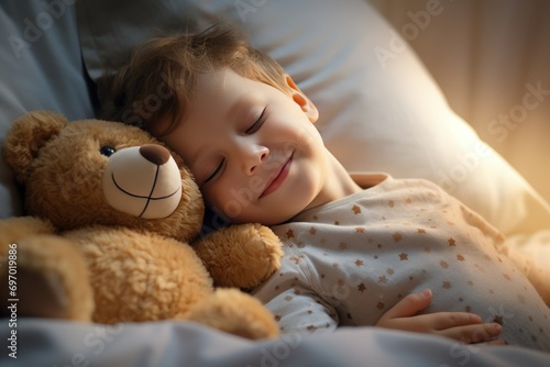 boy sleeps sweetly in bed with a toy bear in his arms under the blanket
