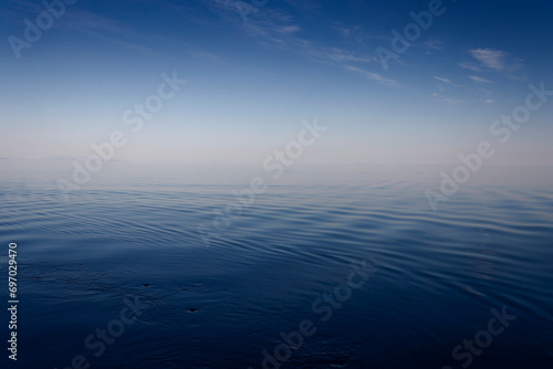 Calm blue sea, blue sky and clouds; summer-warmed haze on the horizon, in the middle of the picture.