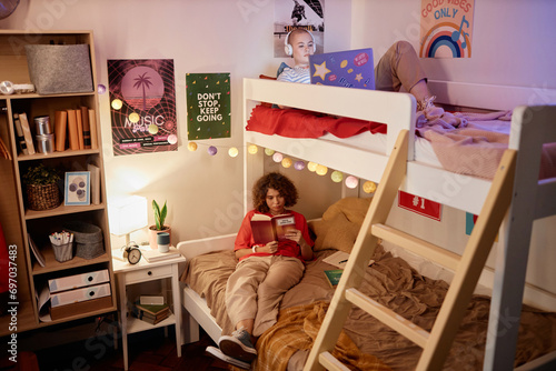 Portrait of two female college students enjoying relaxing evening on bunk bed in dorm room, copy space photo