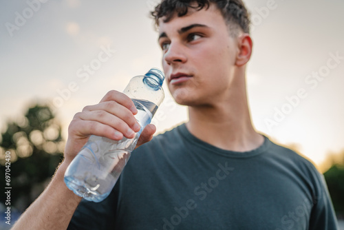 Obraz na plátně caucasian man teenager open plastic bottle of water outdoor in sunny day drink w