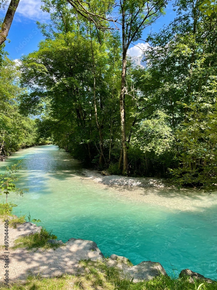 Naklejka premium Blue river at the foot of the mountains in a forest flooded with sunlight
