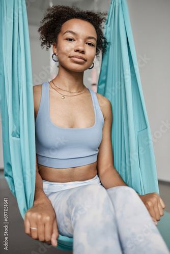 Vertical portrait of young Black woman sitting in hammock and smiling enjoying aerial yoga in studio photo