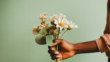 Hand of a Black person holding a bouquet of white daisies against a soft green background.