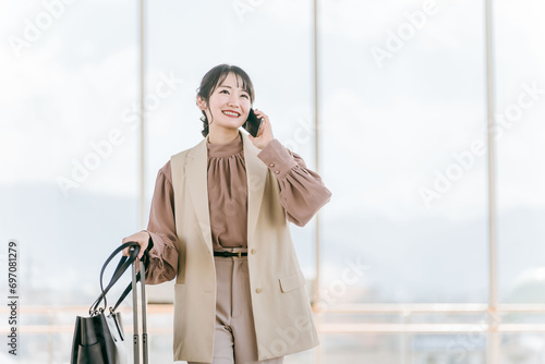 駅ビル・デパート・空港・公共交通機関でスマホで電話する若い女性・旅行するアジア人ビジネスウーマン 