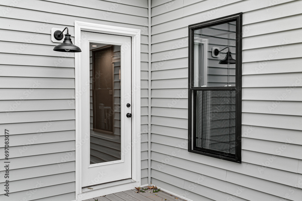 Classic New Home Exterior with Grey Siding Featuring a Door with Glass Panel and A Side Window Under an Outdoor Farmhouse Lamp Classic New Home Exterior with Grey Siding Featuring a Door with Glass Panel and A Side Window Under an Outdoor Farmhouse Lamp