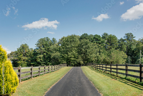 Serene Country Road Flanked by Wooden Fences and Lush Greenery under a Clear Blue Sky  Inviting Scenic Drive into Rural Landscape
