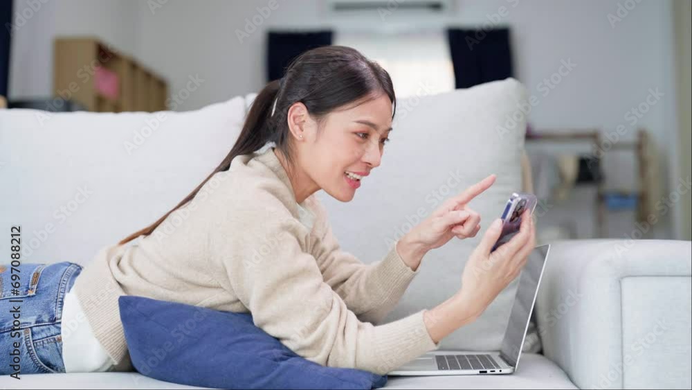 Happy young asian woman relaxing at home. Female smile lying on sofa and holding mobile smartphone. Girl using video call to friend Happy young asian woman relaxing at home. Female smile lying on sofa and holding mobile smartphone. Girl using video call to friend