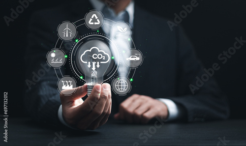 Businessman holding light bulb with CO2 reducing icons for climate change to limit global warming and sustainable development and green business concept.