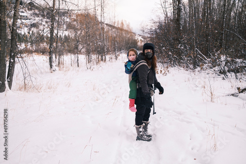 A woman carrying a child in a winter forest hike