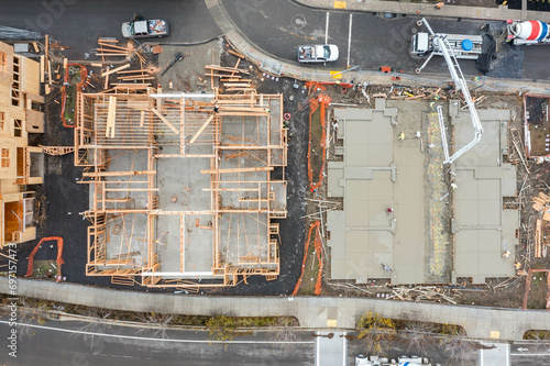 Canvas Print Top down aerial view over a construction site of apartment buildings with framing, concrete and workers wearing protective gear working on site