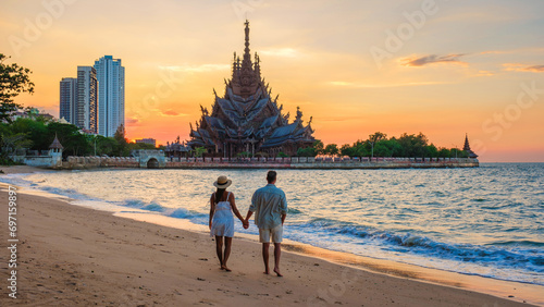 A diverse multiethnic couple of European men and Asian women visit The Sanctuary of Truth wooden temple in Pattaya Thailand at sunset photo