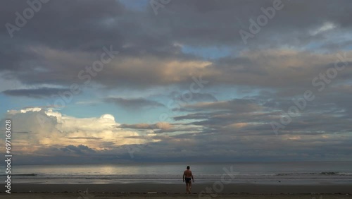 Early morning on a tropical island. Sunrise. The clouds in the blue sky are highlighted in gold. A man walks along a sandy beach towards the ocean, arms outstretched. Malaysia. Borneo. Kota Kinabalu.