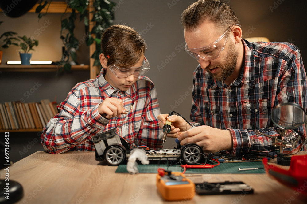 Father teaching his son for soldering remote controlled car in the evening at home. Man and boy fixing broken toy.