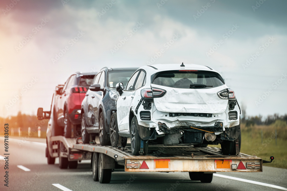 Tow truck carries three cars damaged beyond repair after a severe collision. The insurance company will pay the actual cash value. The cars might be restored or used for parts