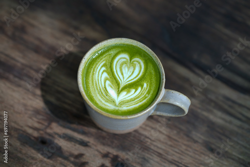 A cup of green matcha latte with heart shaped latte art on wooden table.