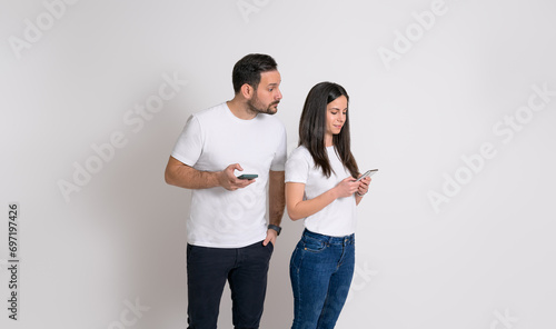 Jealous man peeking into girlfriend's cellphone and trying to read her messages on white background photo