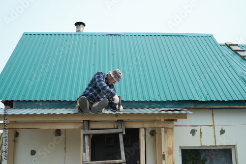 Wallpaper Mural Perched atop his home, a man in work attire installs metal roofing. It's a testament to the importance of maintaining a sturdy shelter. Torontodigital.ca