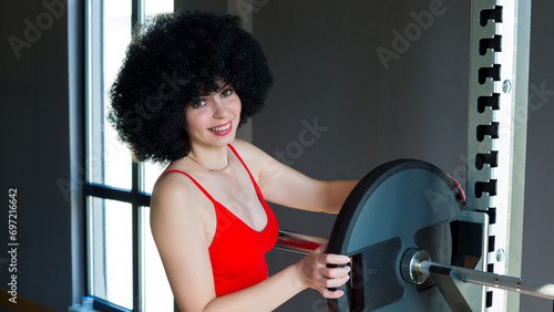 A woman with curly hair puts iron wheel on a sports barbell.