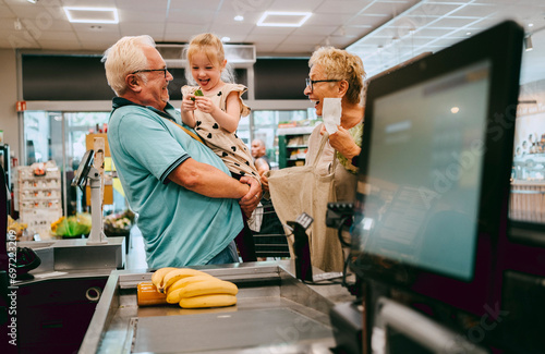 Happy granddaughter having fun with grandparents while shopping at supermarket photo