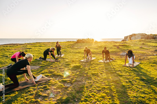Team doing stretching on grass during group training session near sea against sky photo