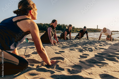 Smiling female instructor doing stretching with team on sand at beach photo