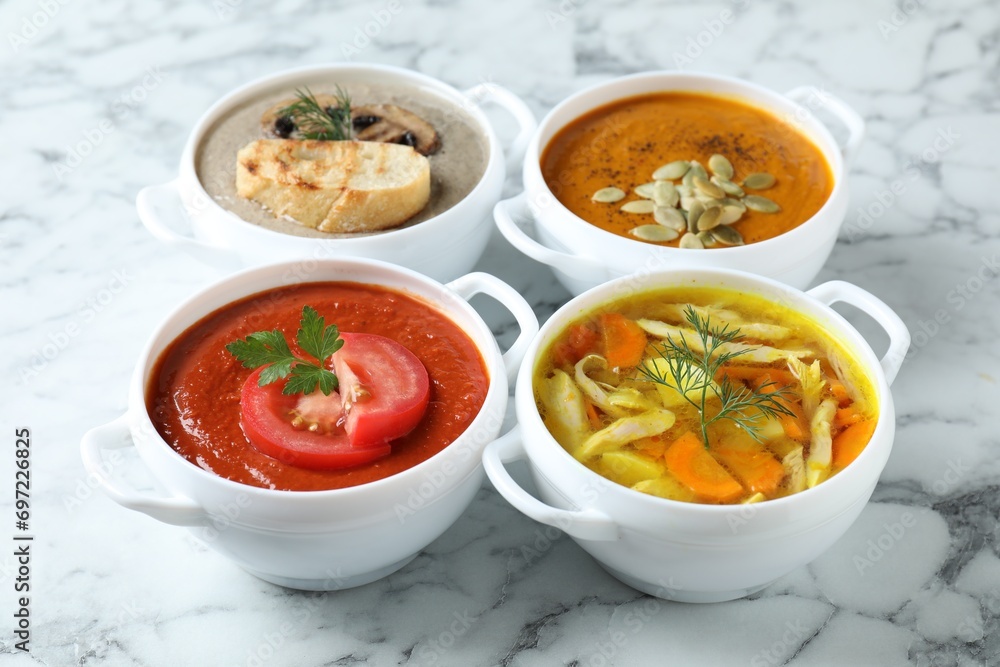 Tasty broth and different cream soups in bowls on white marble table, closeup Tasty broth and different cream soups in bowls on white marble table, closeup