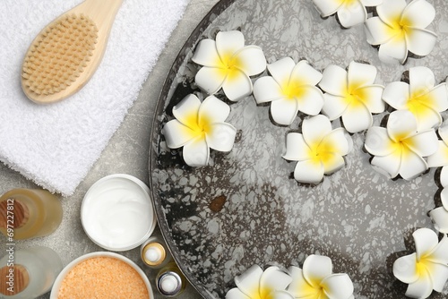 Bowl of water with flowers and different spa supplies on light grey table, flat lay
