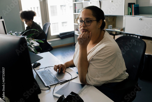 Businesswoman with hand on chin using computer while sitting at desk in office photo