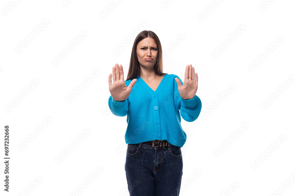 young pretty caucasian woman with black hair dressed in a stylish blue cardigan shows a gesture of disagreement with her hands on a white background young pretty caucasian woman with black hair dressed in a stylish blue cardigan shows a gesture of disagreement with her hands on a white background