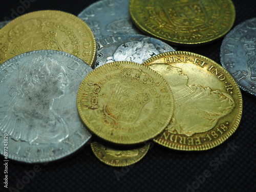 Spanish Escudo and Real coins in gold and silver on a black background