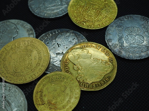 Spanish Escudo and Real coins in gold and silver on a black background