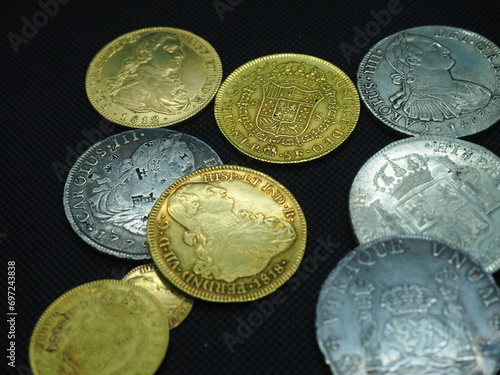 Spanish Escudo and Real coins in gold and silver on a black background