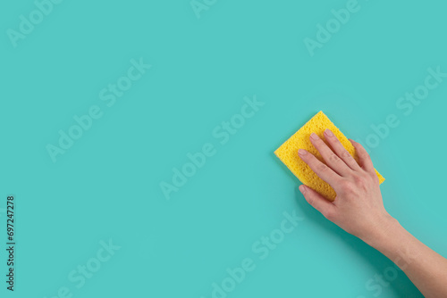 Woman's hand holding washing sponge on blue background. Cleaning concept, professional cleaning, household supplies. Top view with copy space photo
