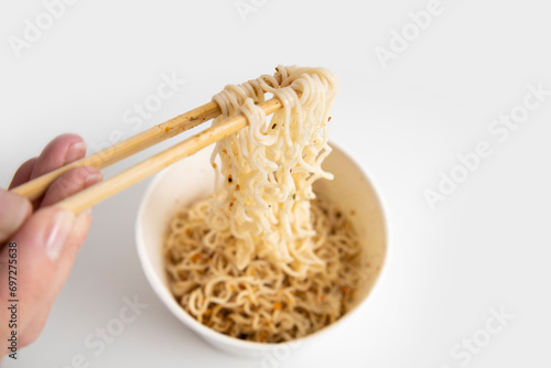 Female hand takes Chinese noodles with Chinese chopsticks from a paper bowl on a white background. Top view, fly lay