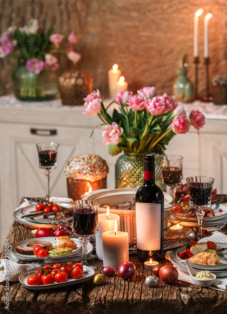 Easter holidays table, wine glasses, Easter cake, color eggs, baked meat with vegetables, flowers and candles for festive dinner at home. Celebration concept