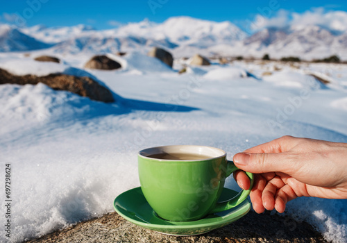 Woman hand holds green teacup on mountains background in winter