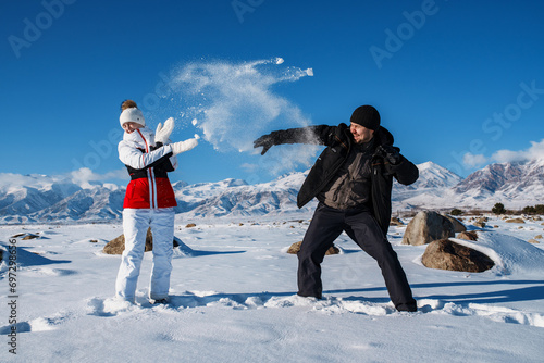 Young man and woman playing snowball on mountains background in winter season