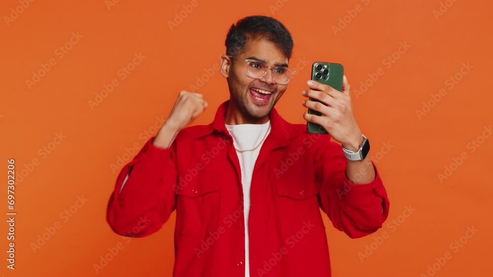 Happy excited Indian young man guy use smartphone typing browsing shouting say wow yes found out great big win good news lottery goal achievement celebrating success, winning play game on orange Happy excited Indian young man guy use smartphone typing browsing shouting say wow yes found out great big win good news lottery goal achievement celebrating success, winning play game on orange