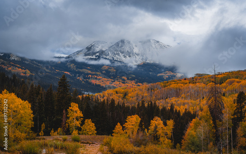 Dramatic Landscape Snow Storm Clouds Over Mountains with Yellow Colored Aspen Tree Forest and Hill in Foreground.