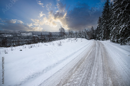 Winter landscape in the sunset. A road full of snow leads through a forest with snow-covered pine trees in Sweden