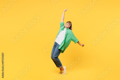 Full body elderly blonde woman 50s year old wear green shirt glasses casual clothes lean back stand on toes with outstretched hands dance isolated on plain yellow background studio. Lifestyle concept photo