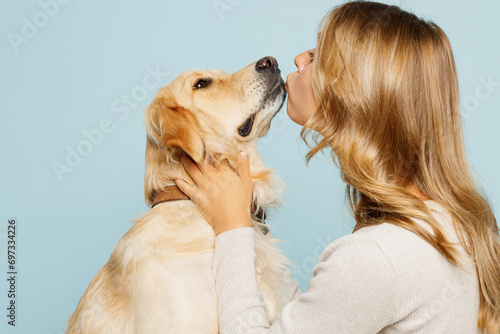 Side profile view young owner woman with her best friend retriever wear casual clothes kiss hug cuddle dog isolated on plain pastel light blue background studio portrait. Take care about pet concept.