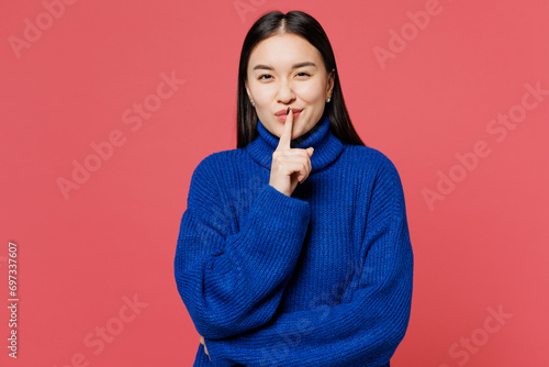 Young secret woman of Asian ethnicity wear blue sweater casual clothes say hush be quiet with finger on lips shhh gesture isolated on plain pastel pink background studio portrait. Lifestyle concept.