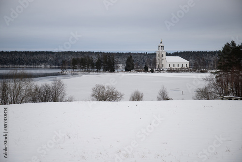 Swedish houses, small white church by a lake in a cold winter landscape with snow and ice. Vårviks kyrka in Sweden © Jan