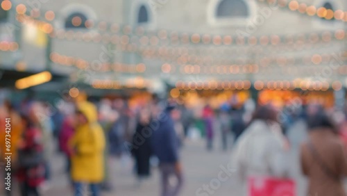 Blurred people walking through Christmas market. Trade tents with lights. Defocused people walk past shopping arcades. Illuminated fair. Background gradually becomes more blurred photo