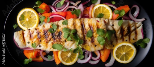 Close up high angle view of grilled pollock or coalfish with colorful salad and lemon slices.