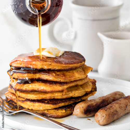 Syrup being poured onto a freshly made stack of sweet potato pancakes.