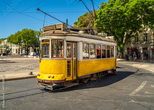Famous and typical old yellow Portuguese tram, beautifully decorated and preserved, running on the tracks of a roundabout of a typical Lisbon street in Portugal.