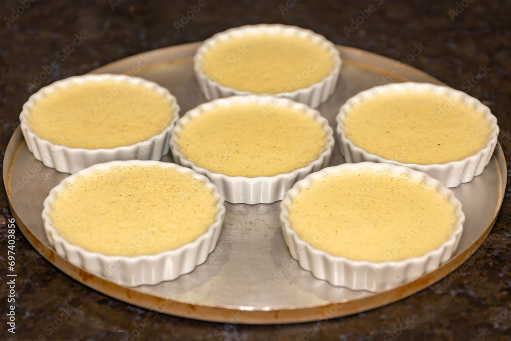 Creme brulee in white ramekins lined with white spoons on rustic background with shallow depth of field blur. Creme brulee in white ramekins lined with white spoons on rustic background with shallow depth of field blur.