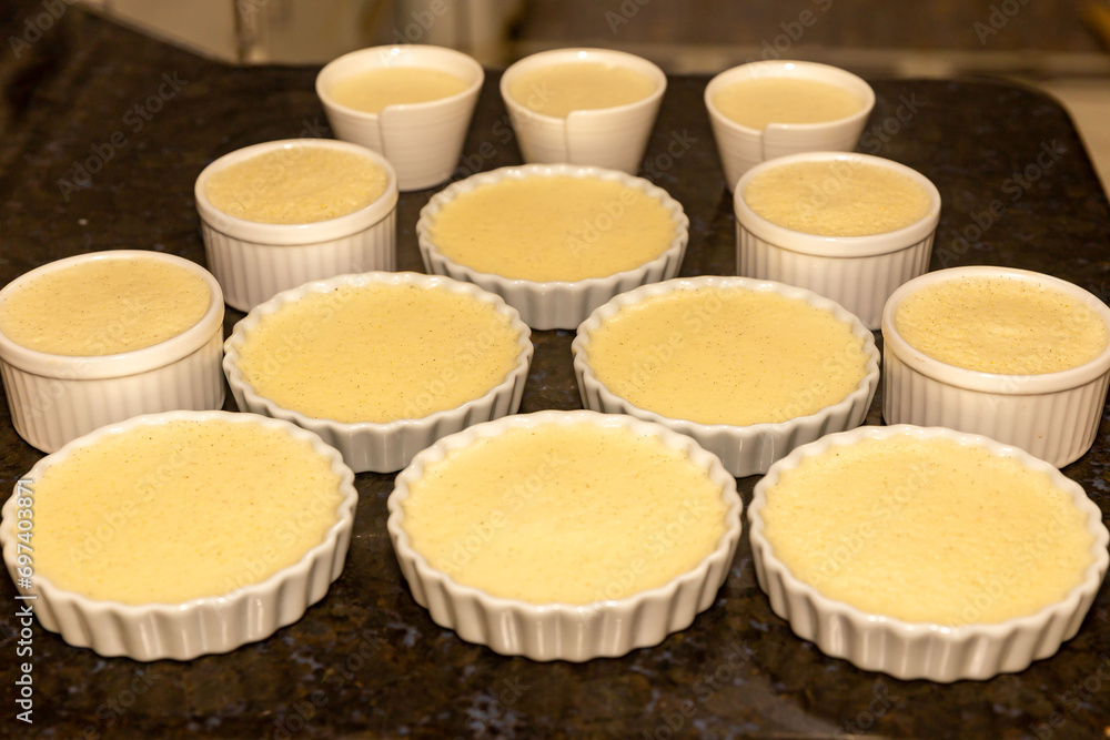 Creme brulee in white ramekins lined with white spoons on rustic background with shallow depth of field blur. Creme brulee in white ramekins lined with white spoons on rustic background with shallow depth of field blur.